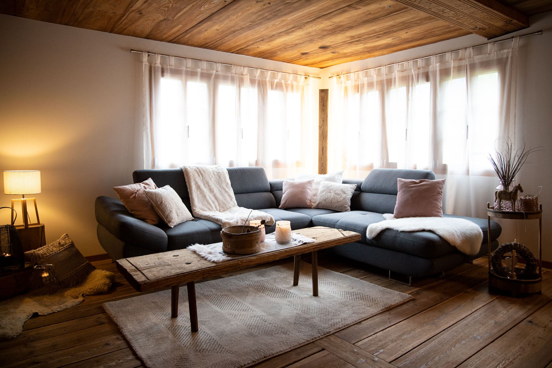 Wohnzimmer mit Sofa, Holztisch, Lammfell und hellen Vorhängen
